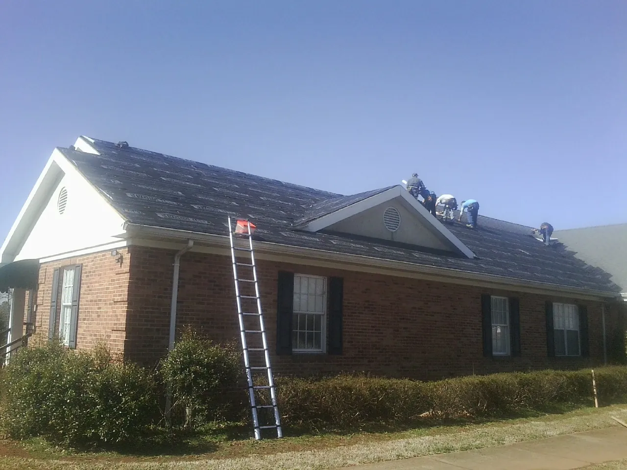 Crew tearing shingles off a brick ranch roof with a ladder set — Metal Roof Repair work by our crew in Penns Grove