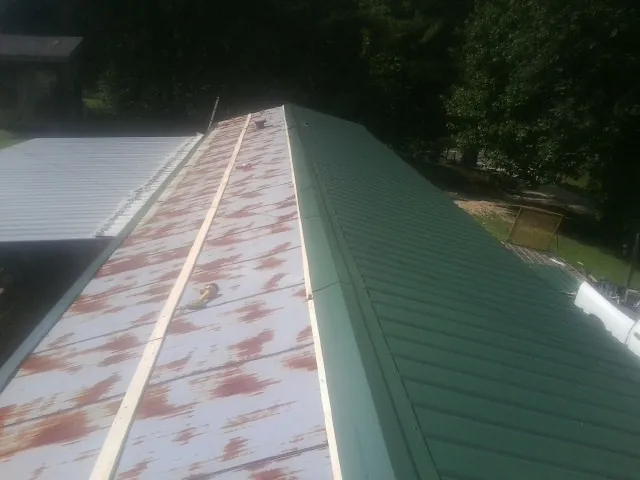 Old rusted panels beside newly installed green metal roofing — Wind Damage Roof Repair by Roofing Brothers in Penns Grove