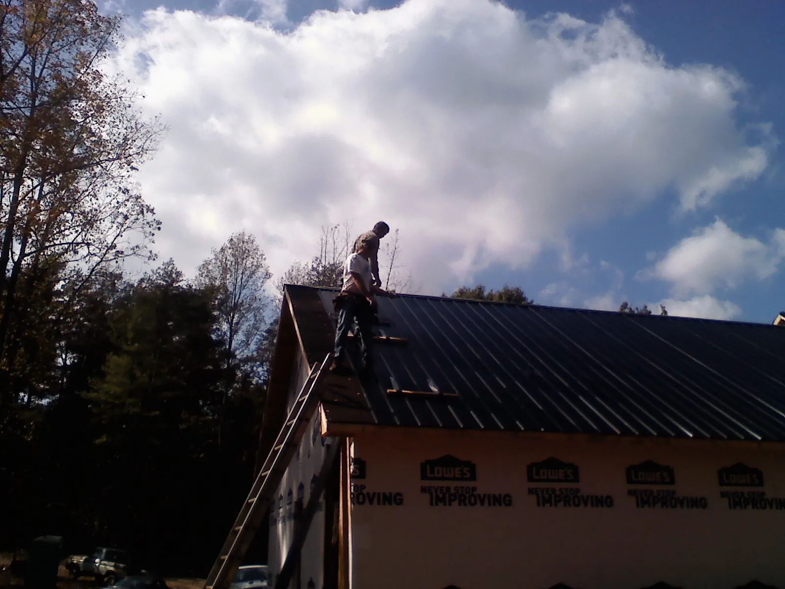 Roofer fastening dark metal panels high against a cloudy sky, from a Roof Inspection job in Penns Grove