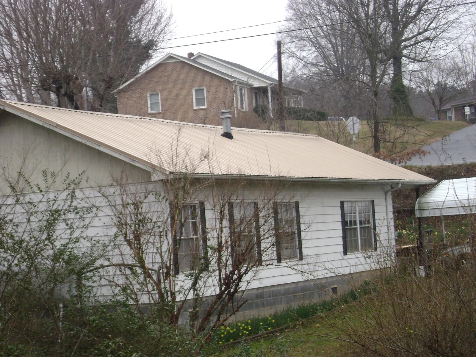 Tan metal roof on a white sided house set into a hillside — Commercial Roofing by Roofing Brothers in Penns Grove